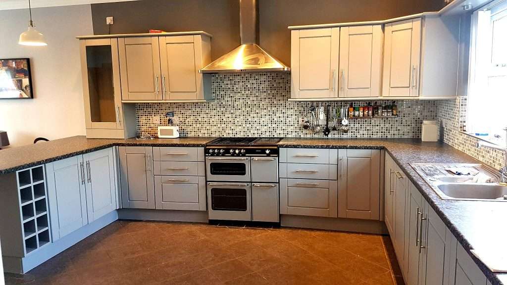 Bright modern kitchen with custom grey cabinets, stylish mosaic backsplash, black granite countertops, and stainless steel appliances in Portstewart.
